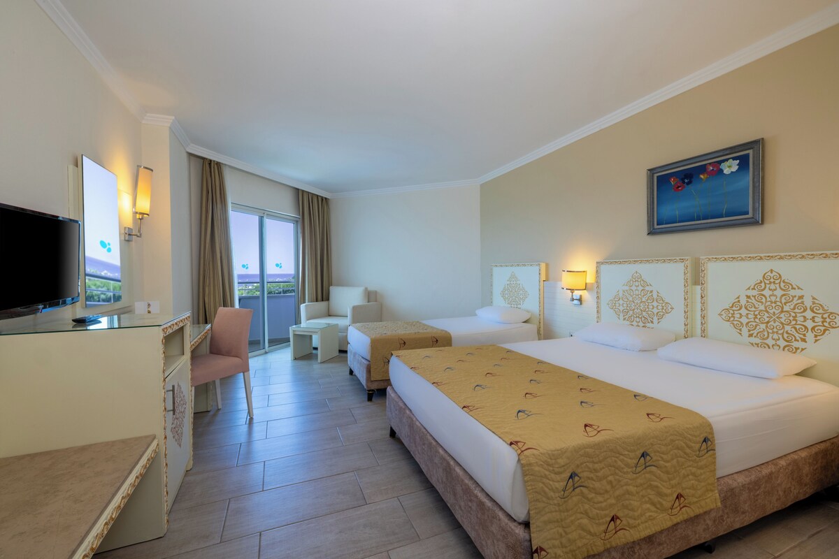 Habitación de hotel con dos camas, un escritorio con televisor, una silla y vistas al exterior.