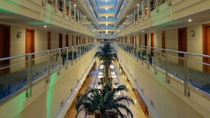 A multi-level hotel interior with a central atrium, glass ceiling, and a palm tree. - Crystal Admiral Aqua Collection - All inclusive (Manavgat)