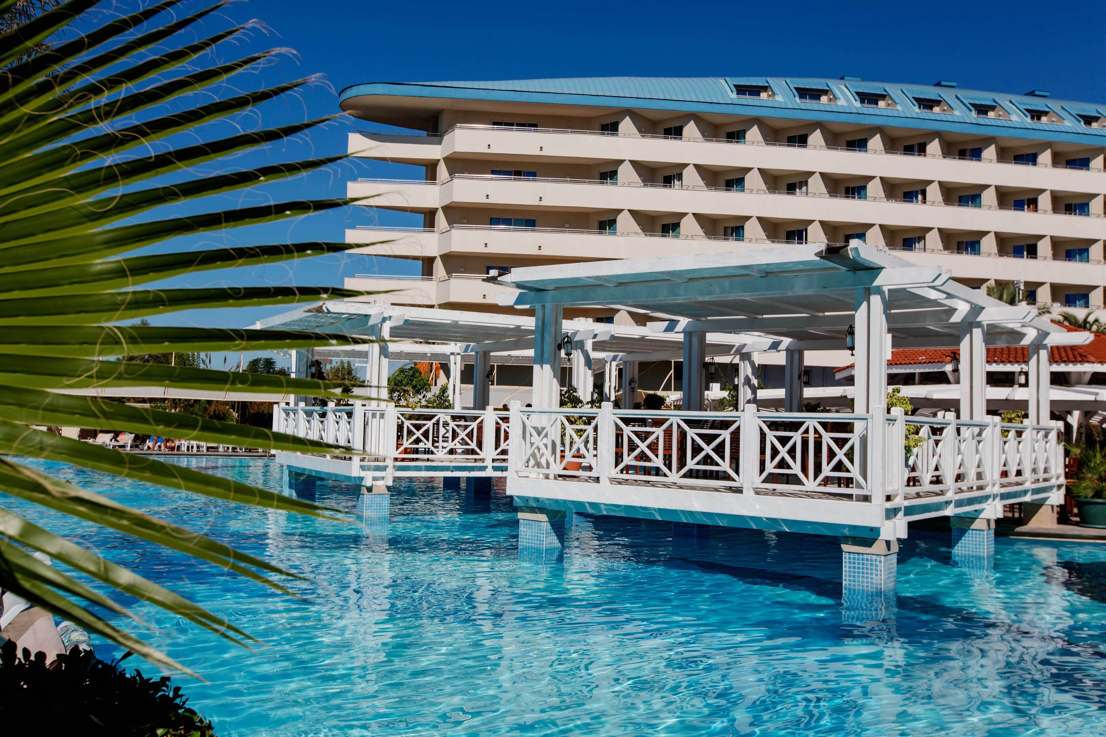A hotel with a large pool, a covered area, and a multi-story building with balconies.