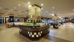 A spacious hotel lobby with a central buffet area, multiple seating arrangements, and a large reception desk. - Crystal Admiral Aqua Collection - All inclusive (Manavgat)