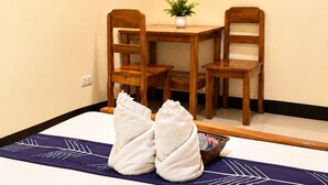 Une chambre d’hôtel avec un lit, deux chaises en bois, une petite table avec une plante, un téléviseur et un panneau indiquant qu’il est interdit de fumer.