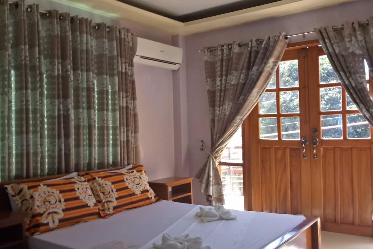 Ein Schlafzimmer mit Bett, Deckenventilator, Vorhängen, Klimaanlage und Holztür.