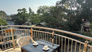 A terrace with a table and chairs, overlooking a street with trees and buildings.