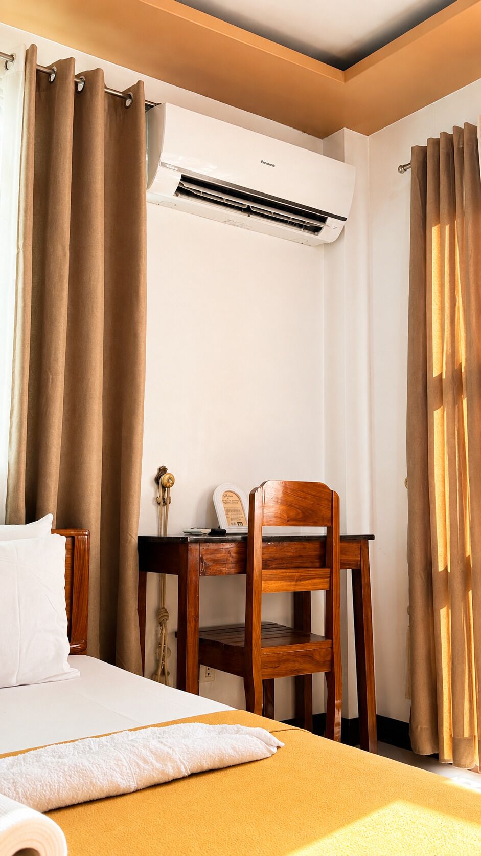 A hotel room with a bed, a desk, a chair, and an air conditioning unit.