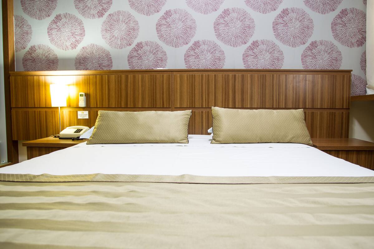 Une chambre d’hôtel avec un grand lit, deux oreillers, une table de chevet avec un téléphone et un mur orné de motifs circulaires.