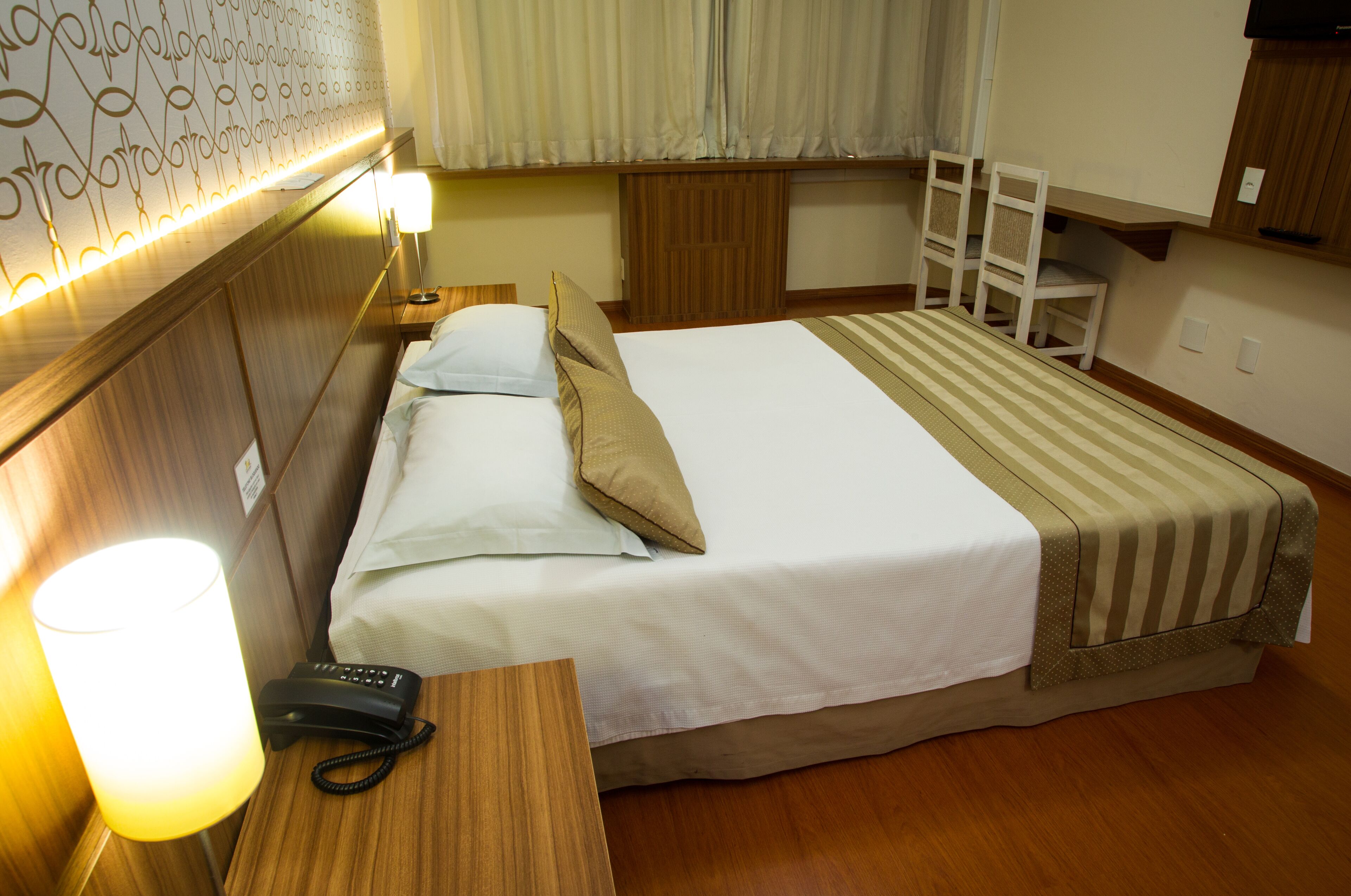Una habitación de hotel con cama, mesita de noche, lámpara y teléfono.