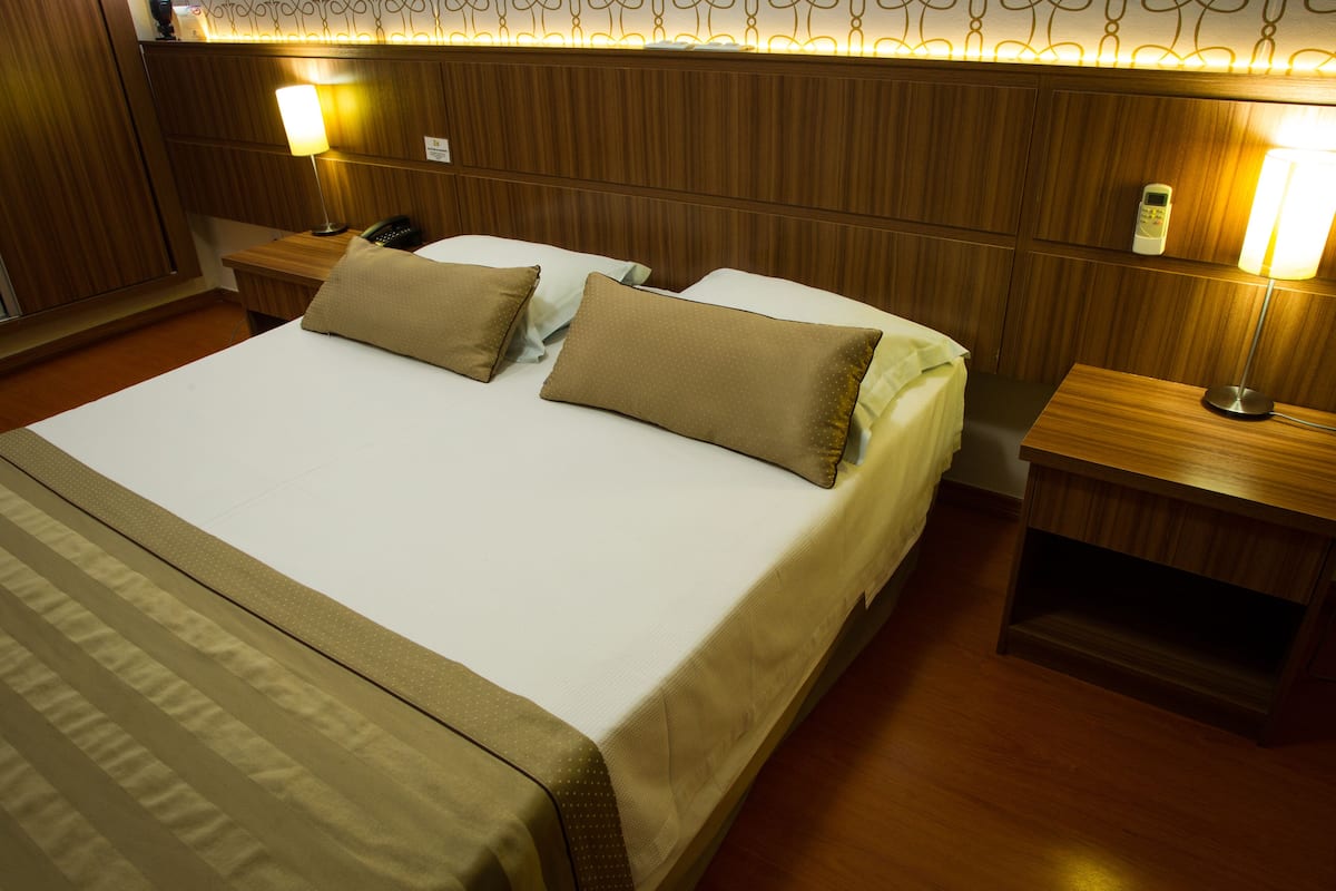 Une chambre d’hôtel avec un grand lit, deux tables de chevet, une petite table et un téléphone fixé au mur.