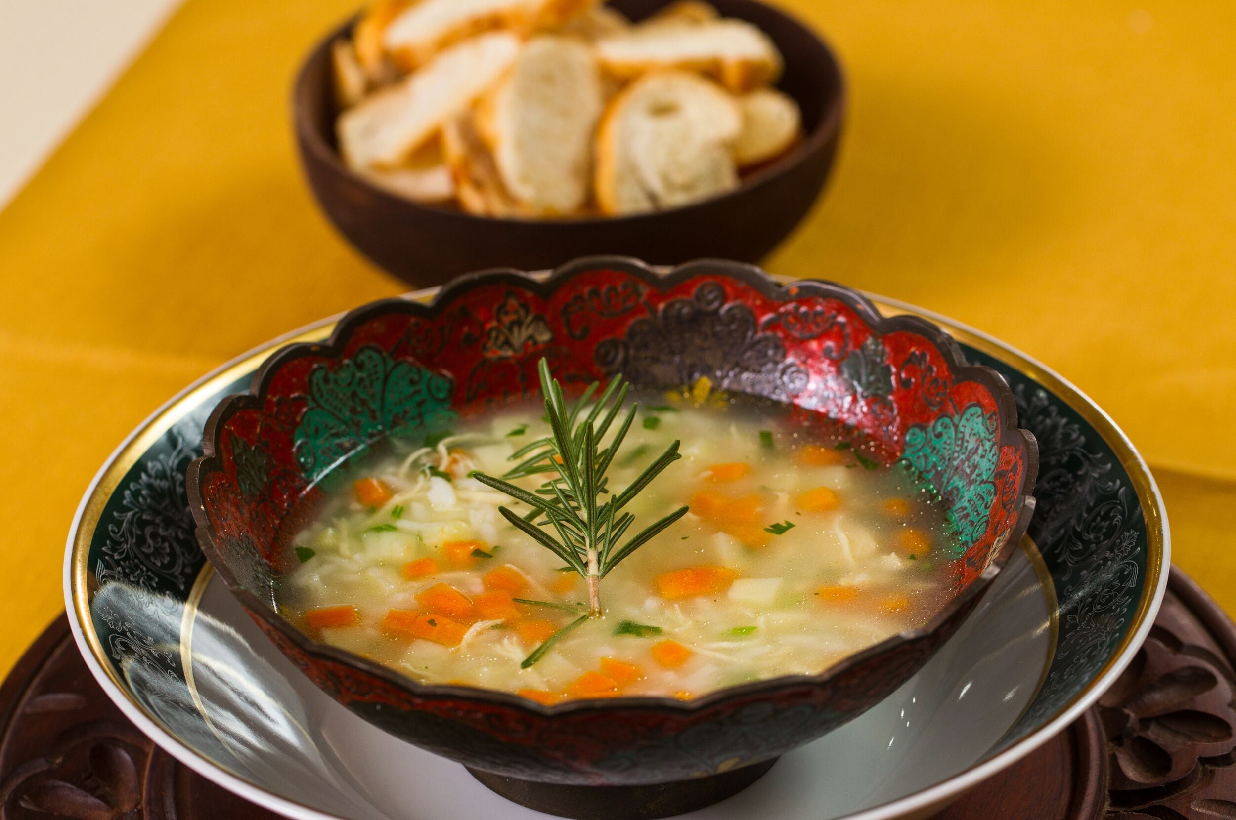 Un plato decorativo con una cazuela de sopa, verduras y una ramita de romero.