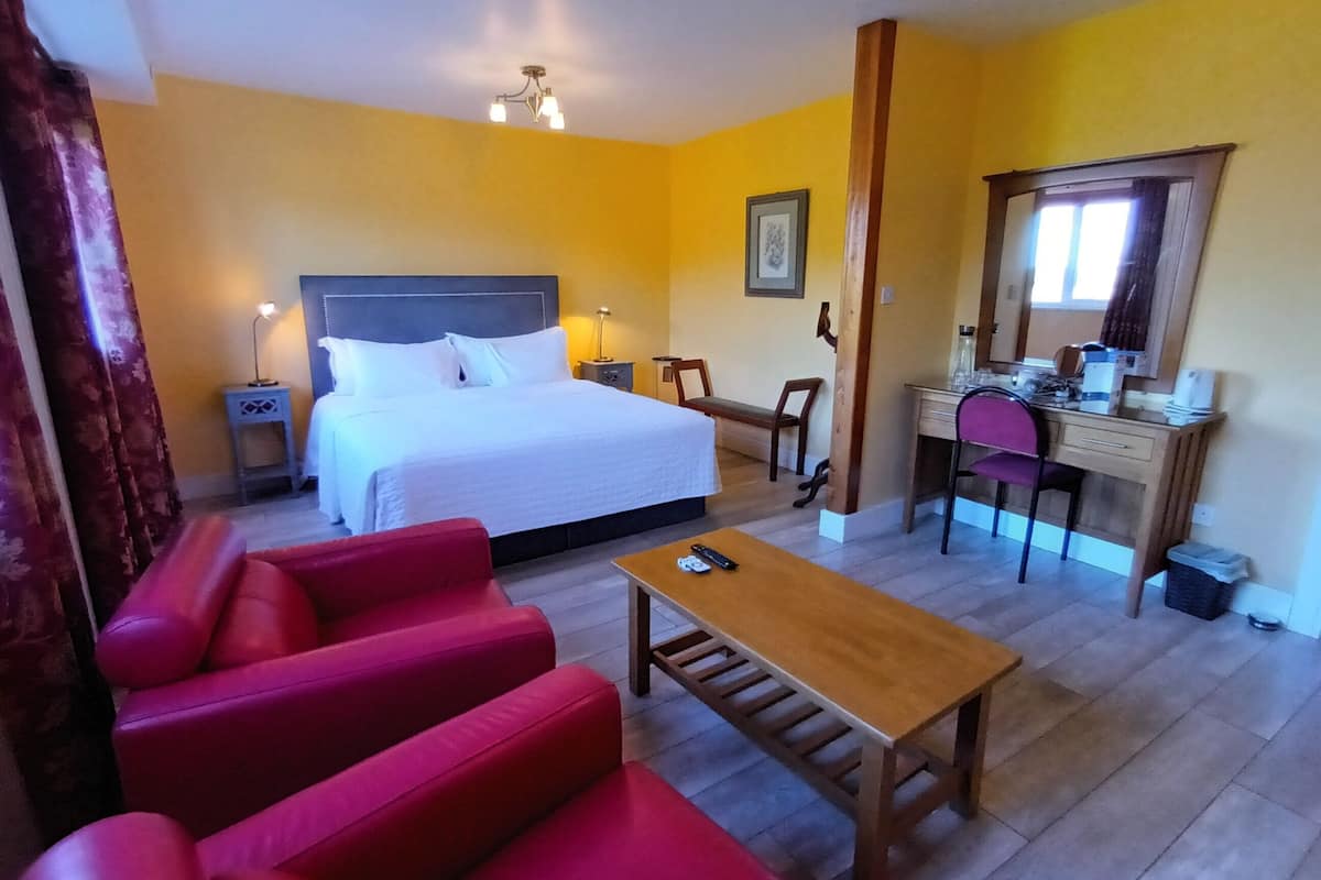 A hotel room with a bed, a desk, a chair, a small table, and a red sofa.