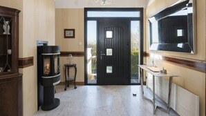 Un pasillo con una puerta negra, una chimenea, un candelabro y un espejo grande.