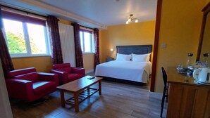 Una habitación de hotel con una cama, un sofá rojo, una mesa de madera y un escritorio con hervidor.