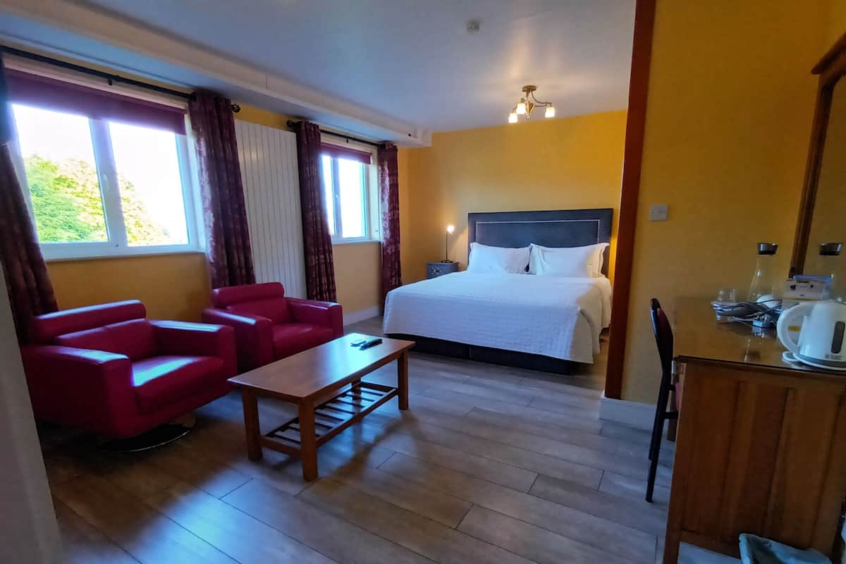 A hotel room with a bed, a red sofa, a wooden table, and a desk with a kettle.