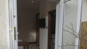 Una puerta que da a una habitación con un banco de madera y un televisor colgado en la pared.