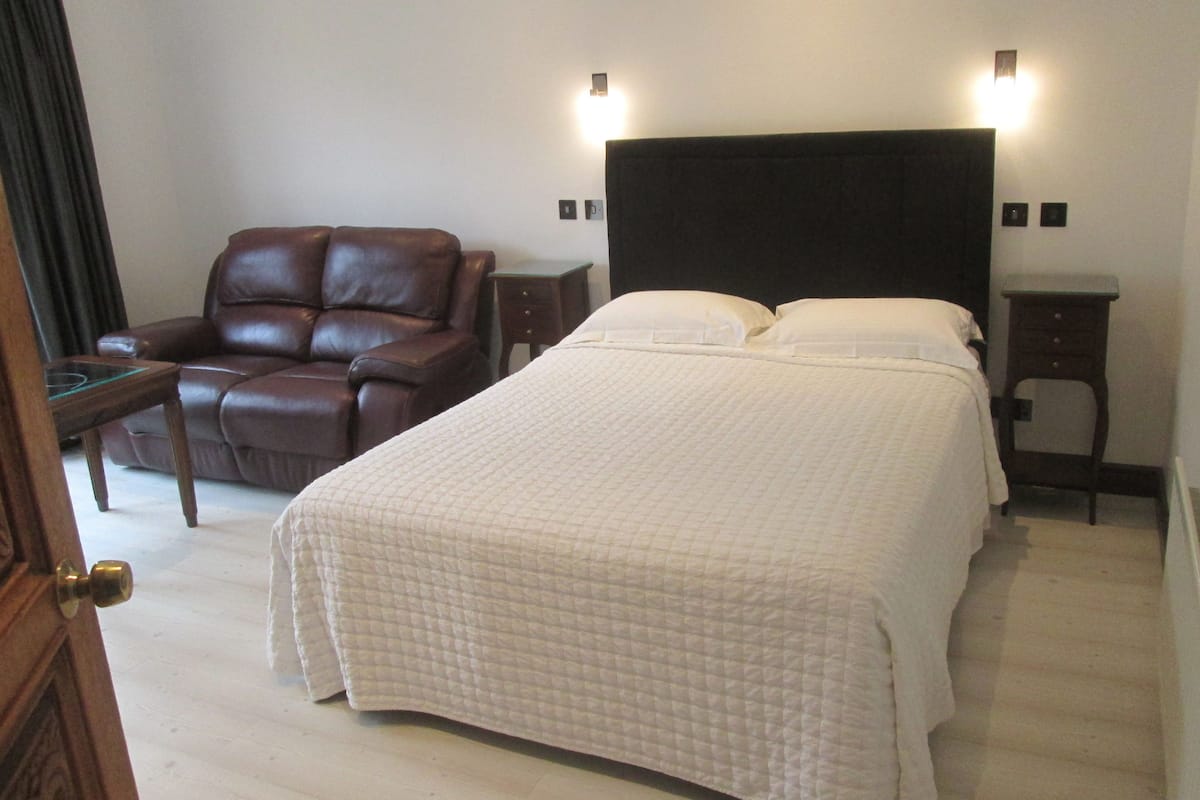A hotel room with a large bed, a leather armchair, a small table, and two bedside tables.