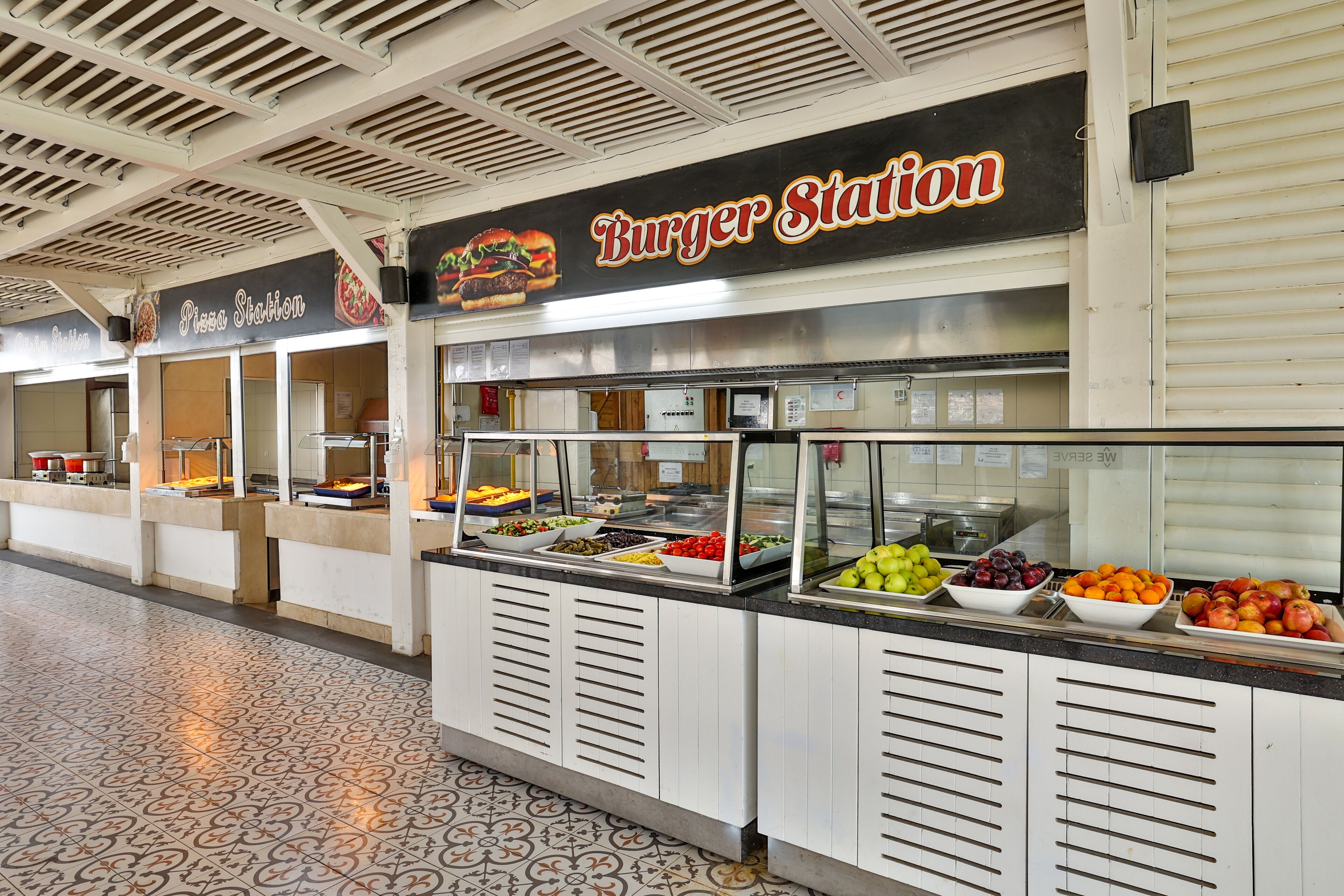 Ein Buffetbereich mit einer Burger-Station und einer Pizza-Station, mit verschiedenen Speisen und einem gemusterten Boden.