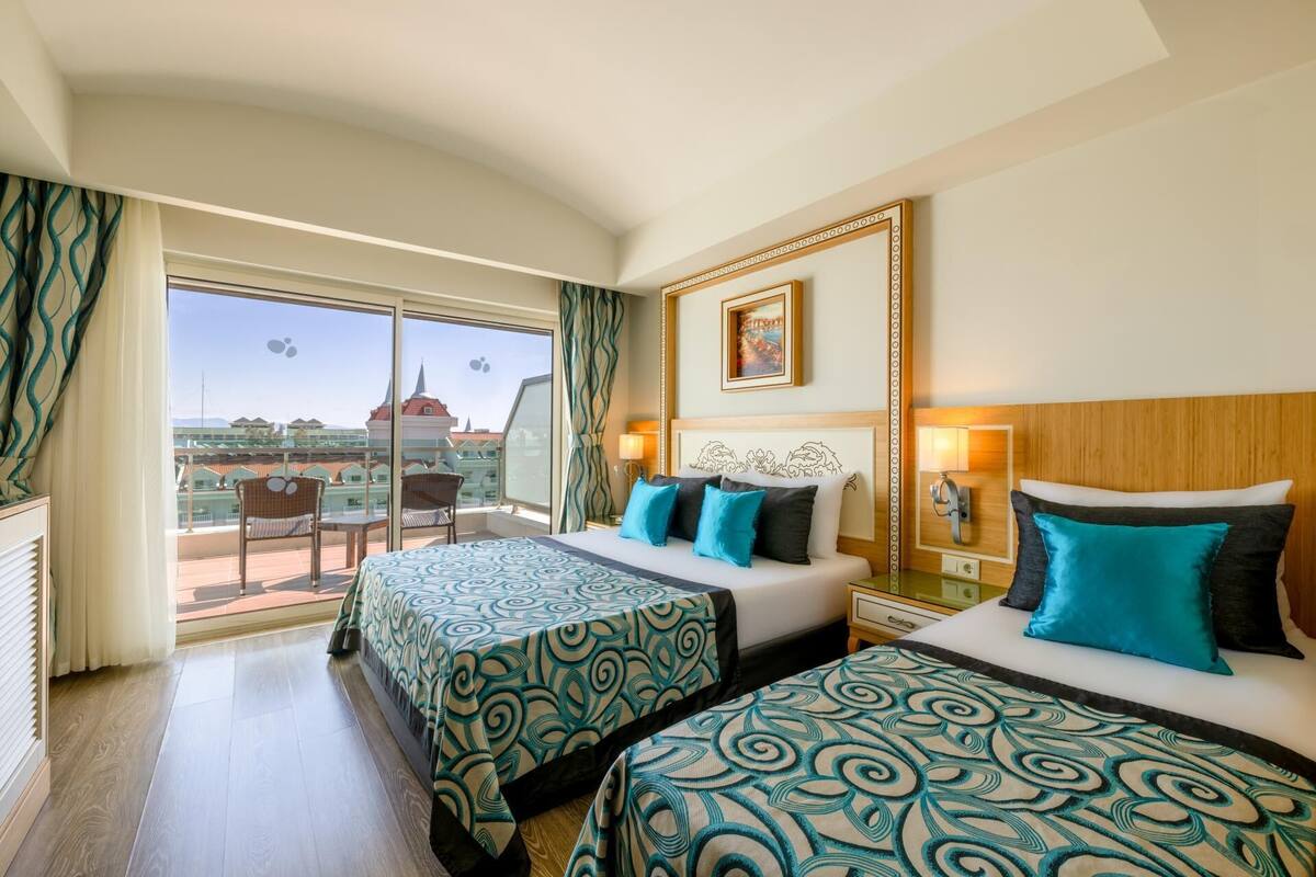A hotel room with two beds, a balcony with a view, and a painting on the wall.