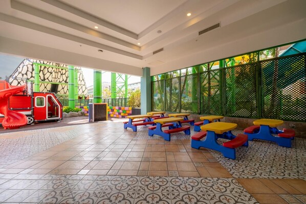A children's play area with a slide and climbing structure, outdoor seating with colorful tables and benches, and a patterned tiled floor. - Crystal Waterworld Aqua Collection - All inclusive (Serik)