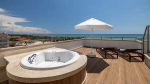 Une terrasse sur le toit avec un jacuzzi, des chaises longues et une vue sur l’océan.