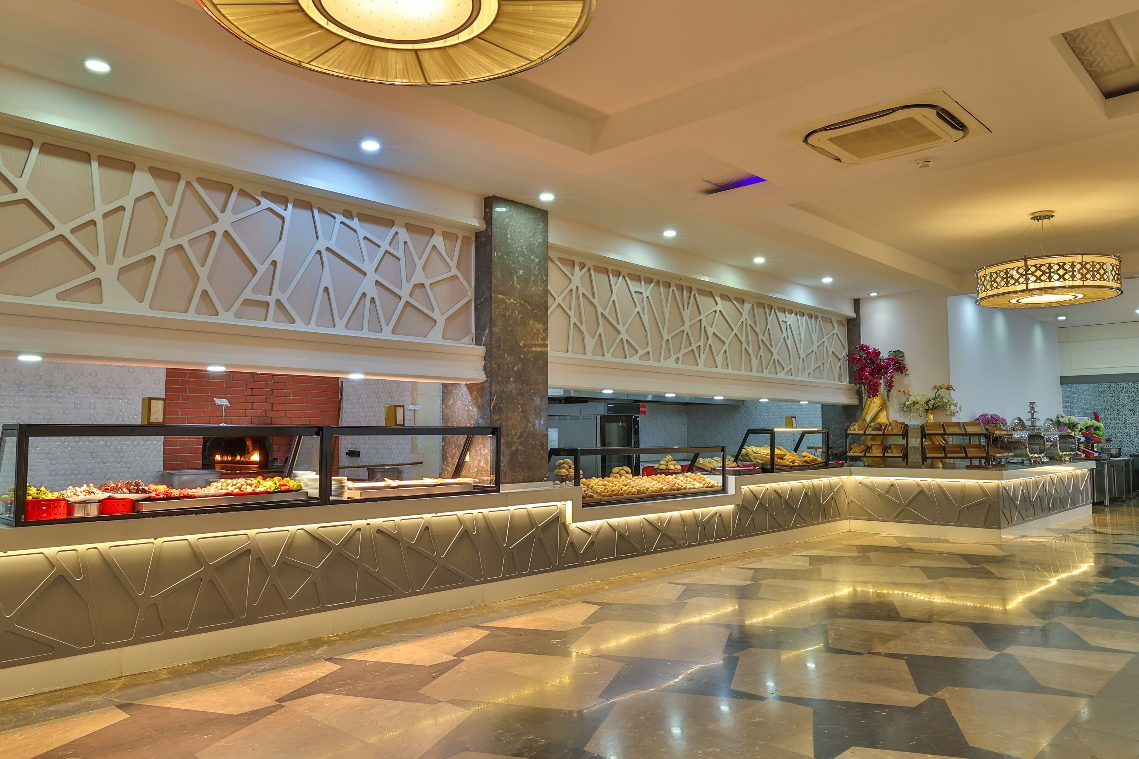 Un hall d’entrée spacieux au design moderne, avec une colonne centrale, un espace buffet proposant divers plats et un plafond décoratif agrémenté d’un éclairage aux motifs originaux.
