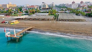 Vue aérienne d’un complexe hôtelier situé en bord de mer, avec une jetée, des chaises de plage et des parasols.