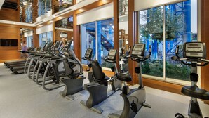 Une salle de sport équipée de nombreux appareils d’exercice, dotée de grandes fenêtres et offrant une vue sur une zone industrielle.