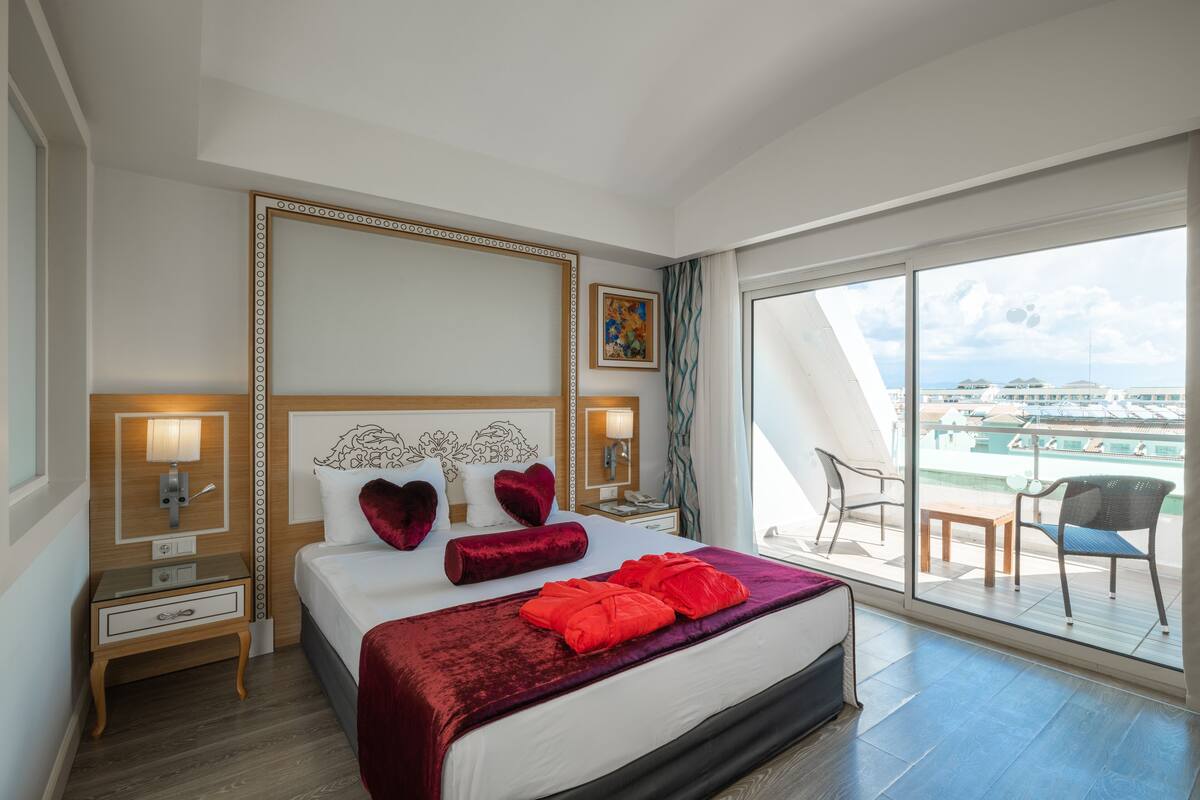 A hotel room with a large bed, a balcony with a view, and a painting on the wall.