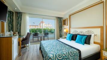 Ein Hotelzimmer mit Bett, Schreibtisch, Stuhl, Fernseher und einem Balkon mit Blick auf Gebäude.