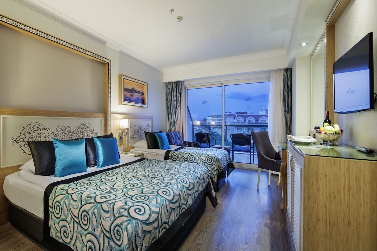 A hotel room with two beds, a desk, a TV, and a view of the cityscape.