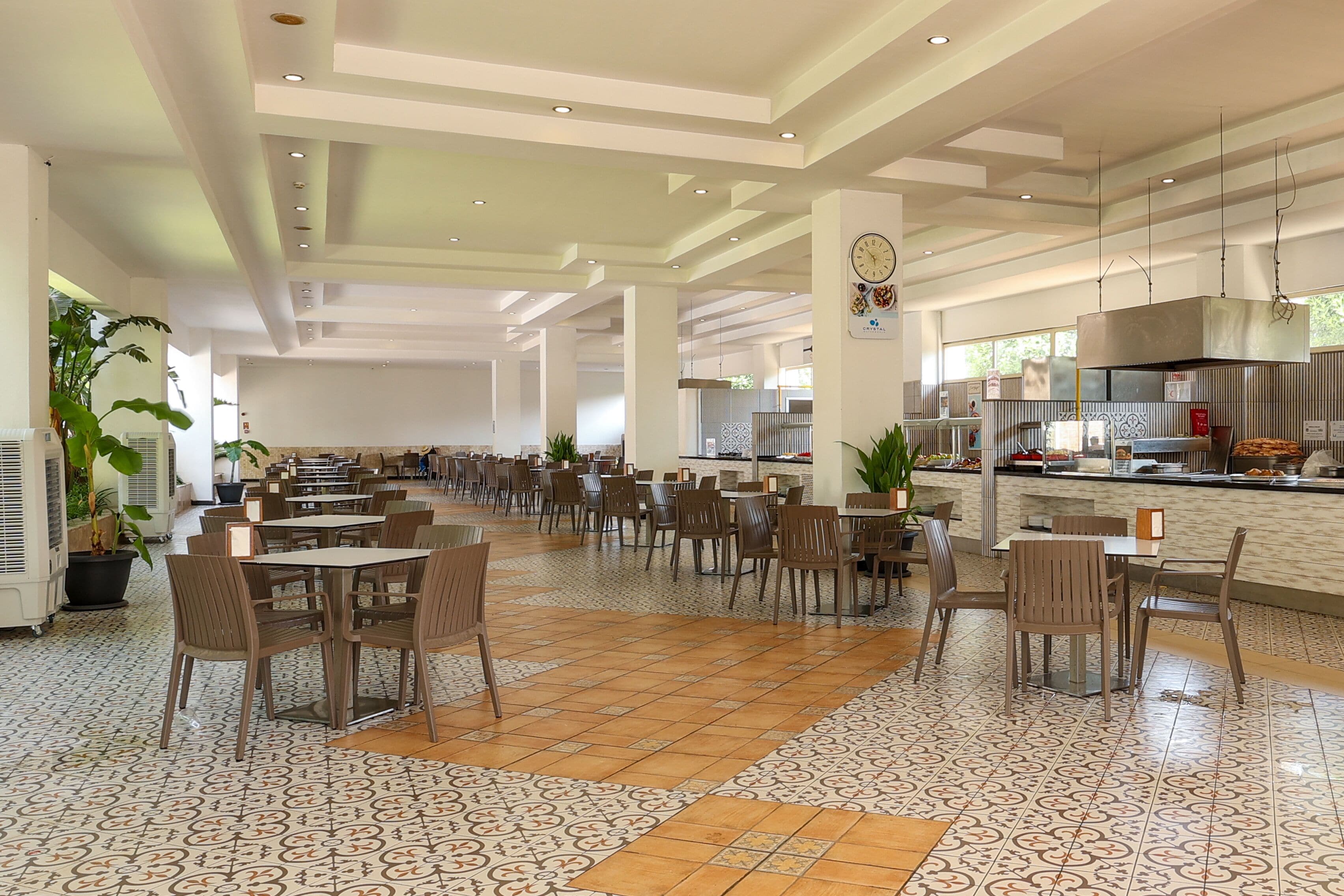 A spacious indoor dining area with multiple tables and chairs, a kitchen area with a buffet, and large windows allowing natural light.