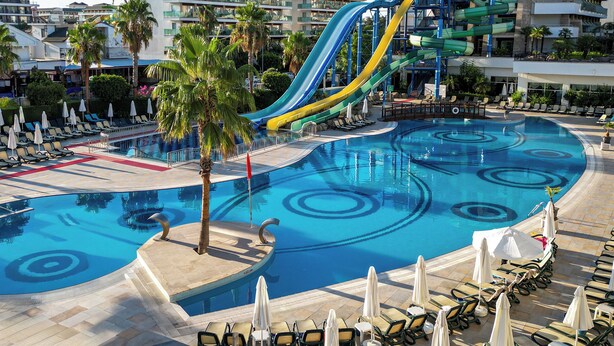 Une piscine avec un toboggan, des chaises longues et des palmiers.