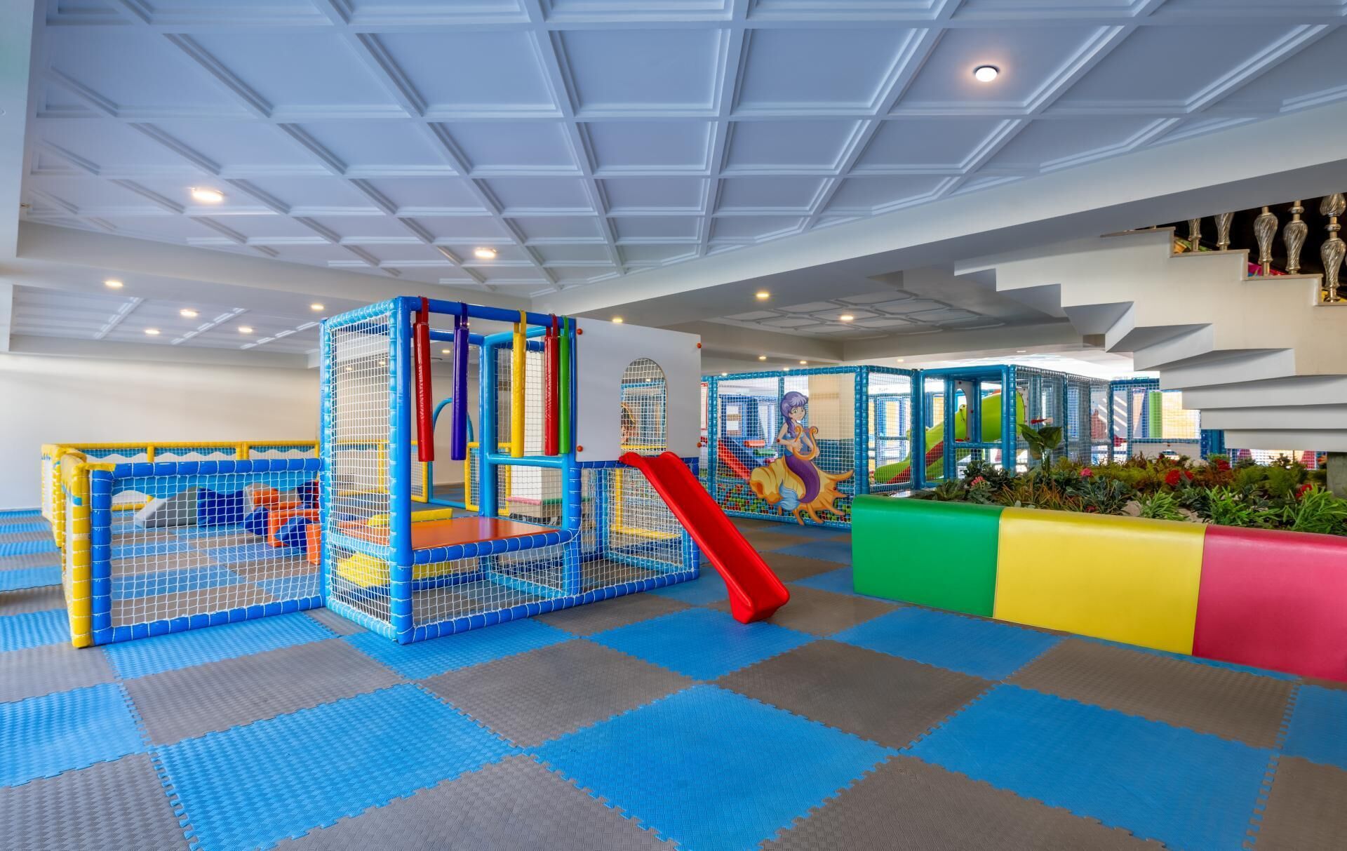 A children's play area with a climbing structure, slides, and padded flooring.
