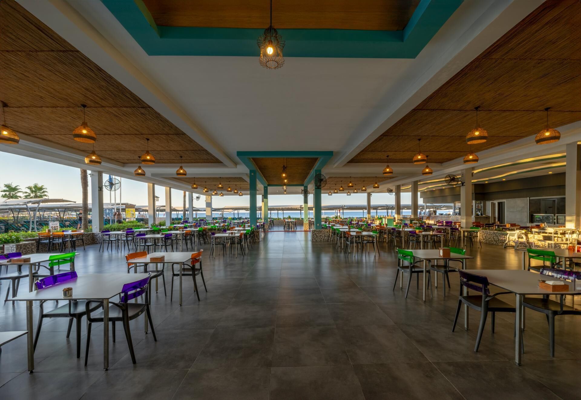 A spacious indoor dining area with multiple tables and chairs, large windows, and a view of the sea.