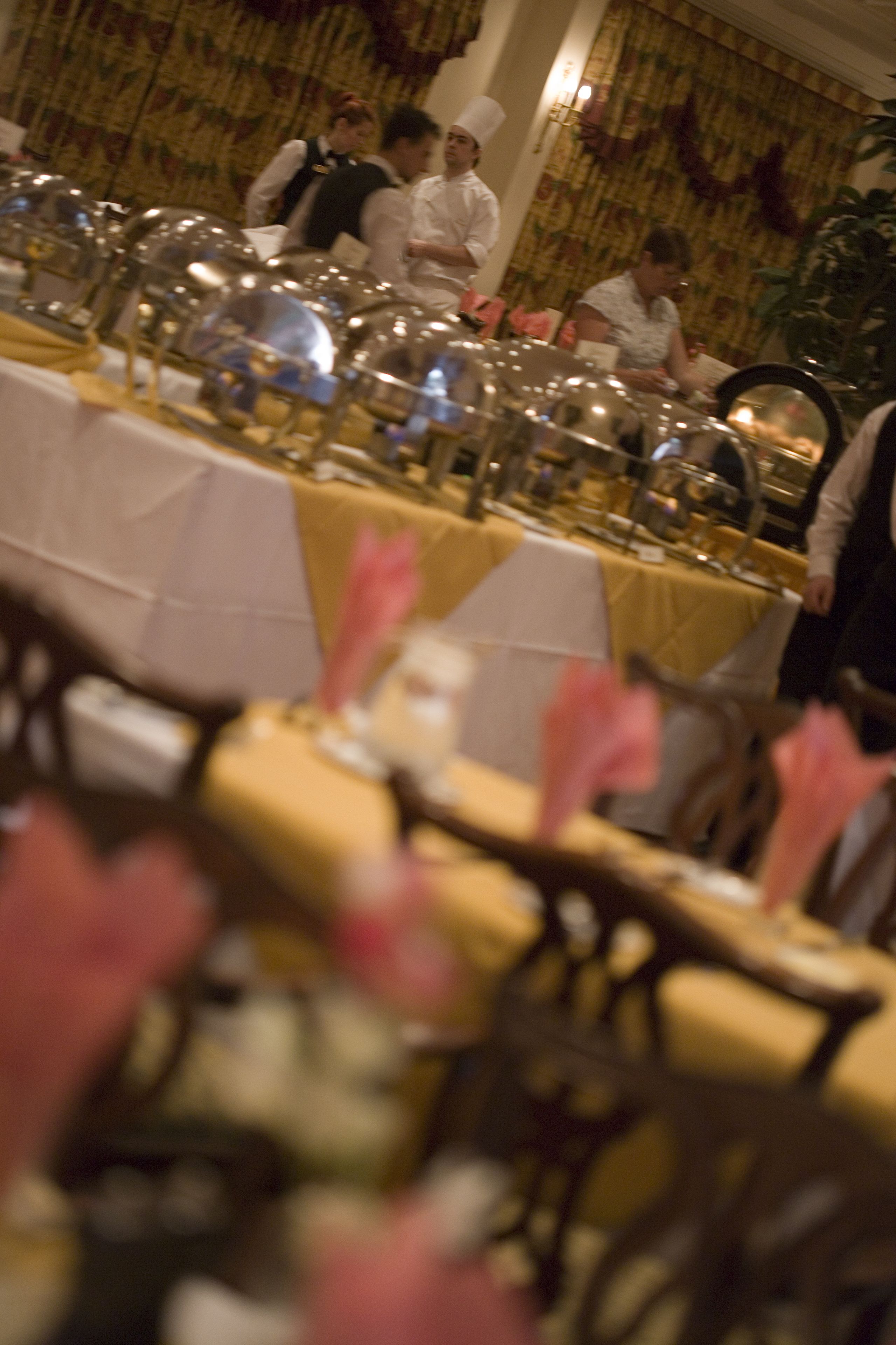 A banquet hall with tables set for a formal event, featuring a long table with multiple place settings and a smaller table with a few chairs.