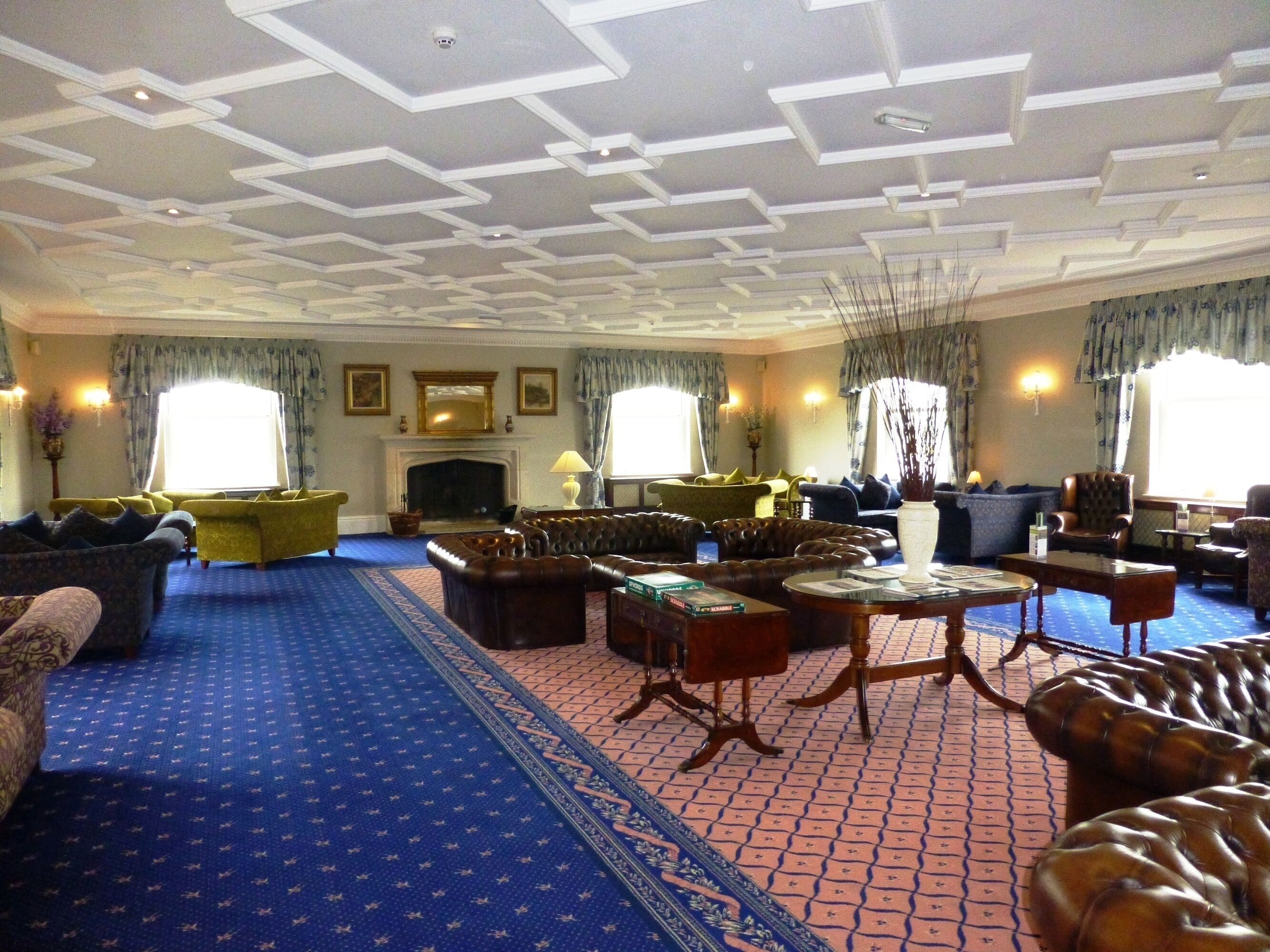 A spacious living room with a patterned carpet, leather sofas, and a fireplace.