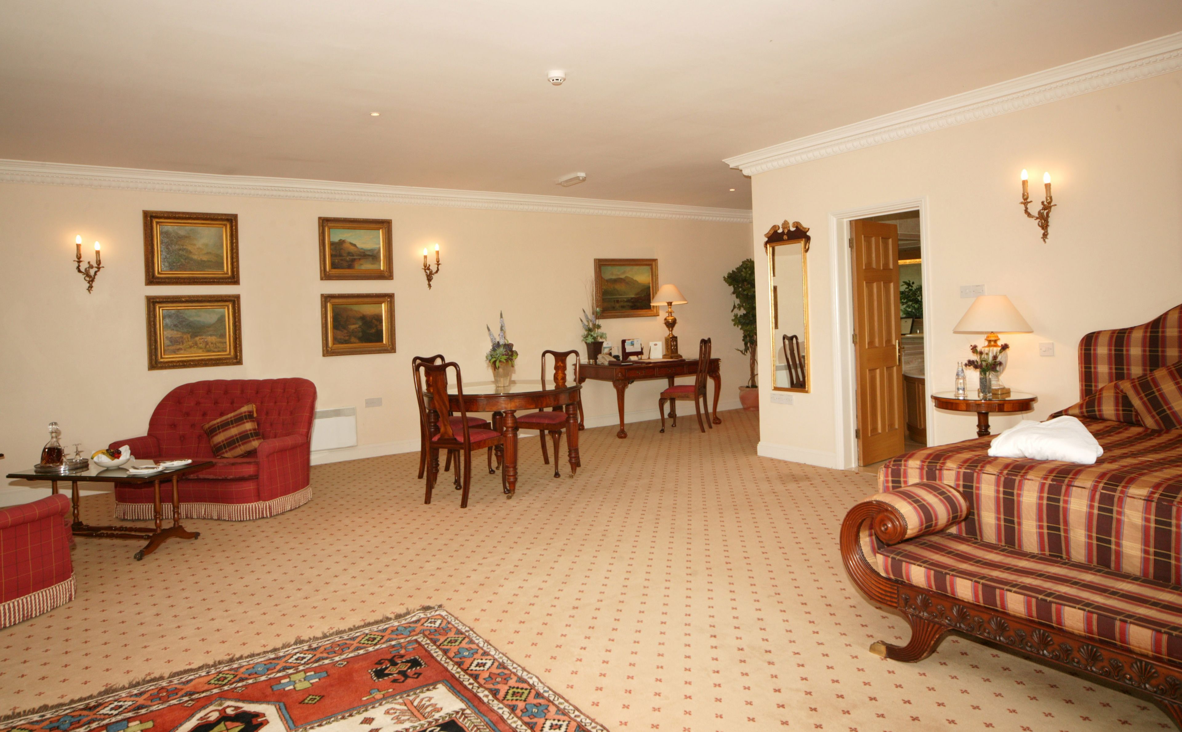 A hotel room with a red sofa, a plaid sofa, a dining table with chairs, and a carpeted floor.