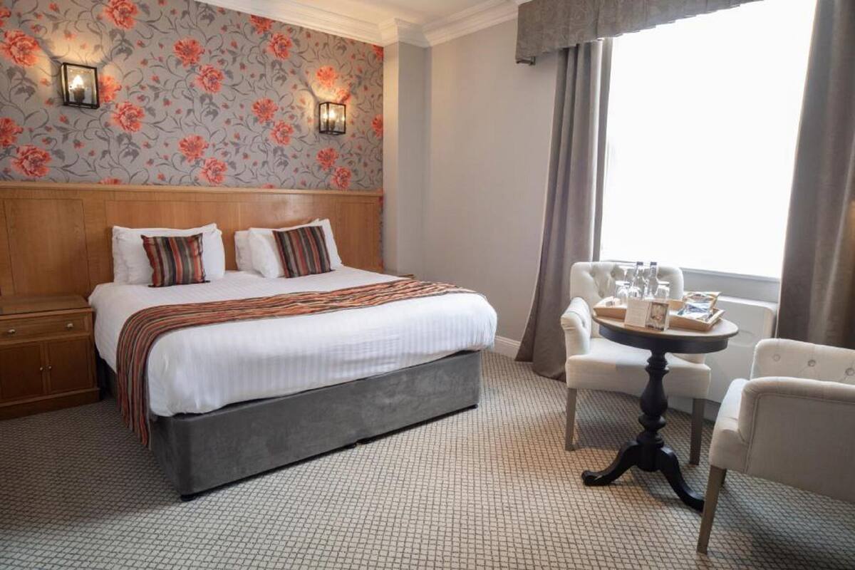 A hotel room with a large bed, a wooden headboard, a small round table with a tray, and a chair.