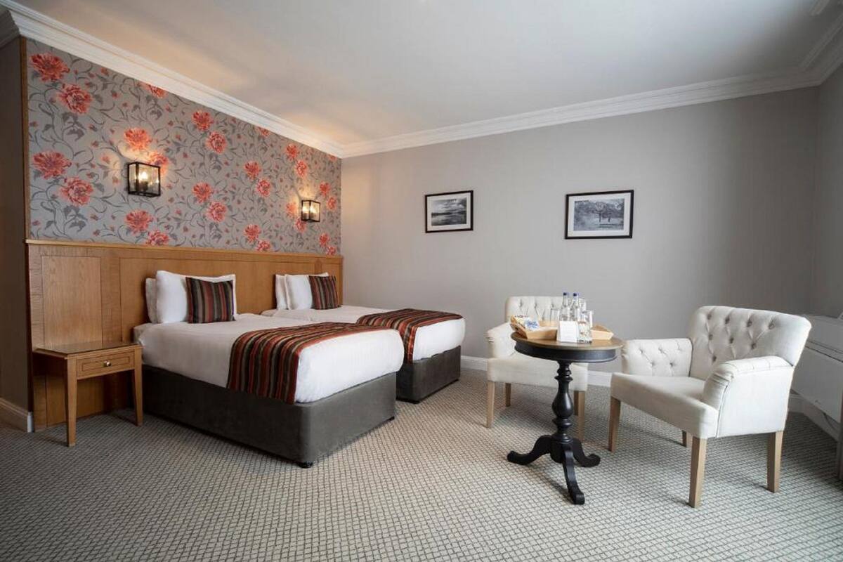 A hotel room with a large bed, two bedside tables, a round table with chairs, and floral wallpaper.