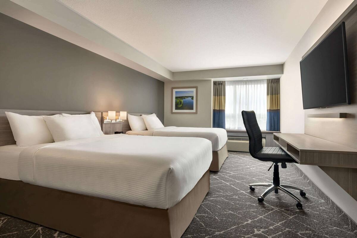 Une chambre d’hôtel avec deux lits, un bureau, une chaise, un téléviseur à écran plat et une fenêtre avec des rideaux.