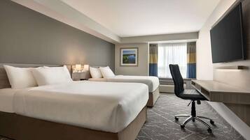 A hotel room with two beds, a desk, a chair, a flat-screen TV, and a window with curtains.