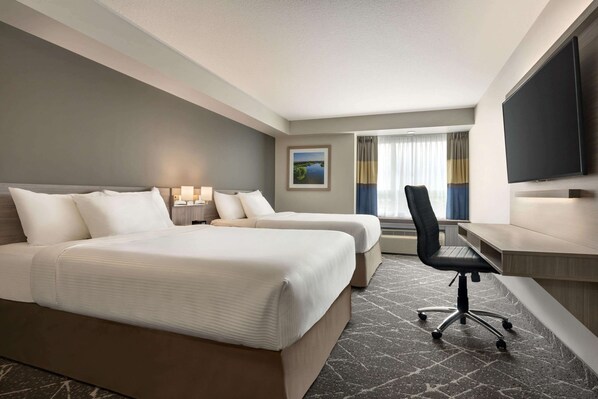 Une chambre d’hôtel avec deux lits, un bureau, une chaise, un téléviseur à écran plat et une fenêtre avec des rideaux.