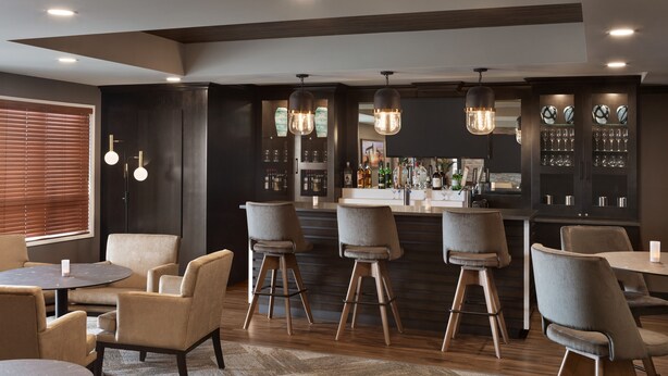 Zona de bar moderna con taburetes, una barra y una variedad de botellas y vasos.