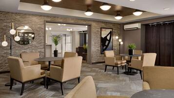 A modern lobby with beige armchairs, round tables, and a stone-textured wall.