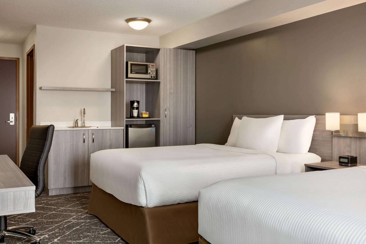 Une chambre d’hôtel avec deux lits, un bureau, un mini-bar, un four à micro-ondes et une machine à café.