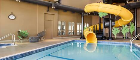 Una piscina interior con un tobogán amarillo, zona de estar y un reloj en la pared.