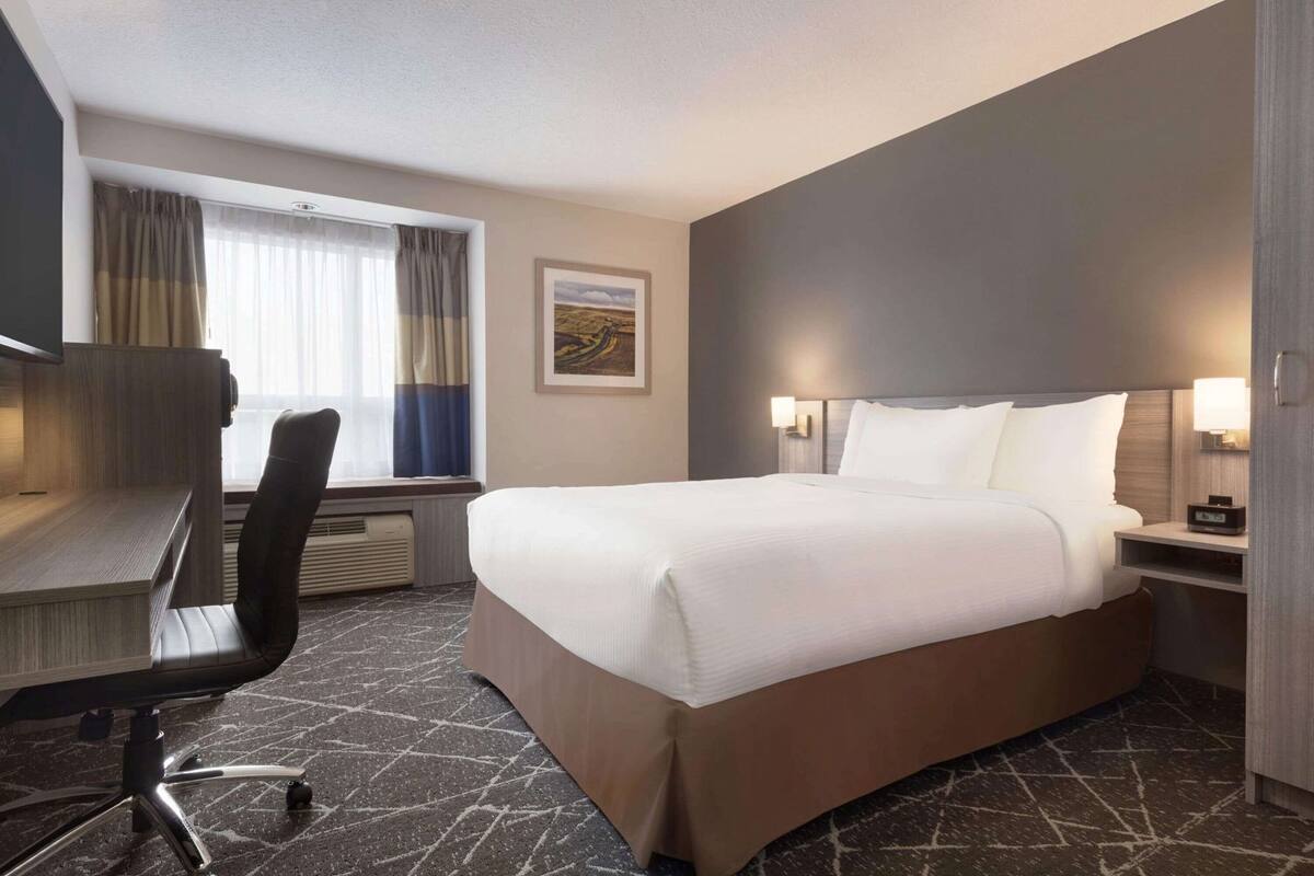 Une chambre d’hôtel avec un lit, un bureau, une chaise et une fenêtre avec des rideaux.