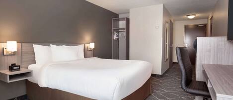 Habitación de hotel con una cama grande, un escritorio y una silla. Se observa un armario y un espejo en la pared.