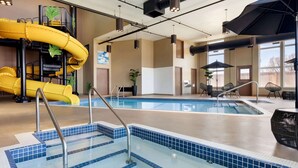 Una piscina con baldosas azules cristalinas, un tobogán amarillo y una zona de estar con sombrillas.