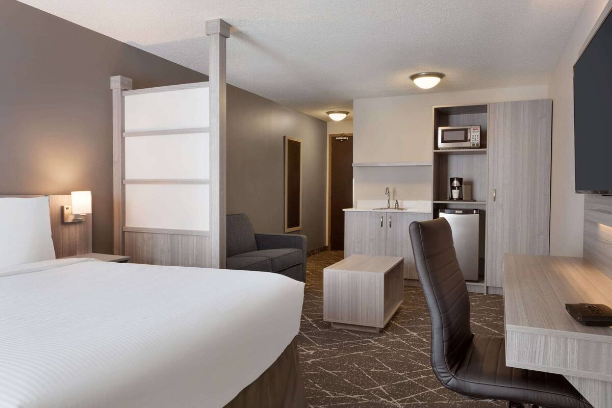 Une chambre d’hôtel avec un grand lit, un bureau avec une chaise, un four à micro-ondes et un petit placard.