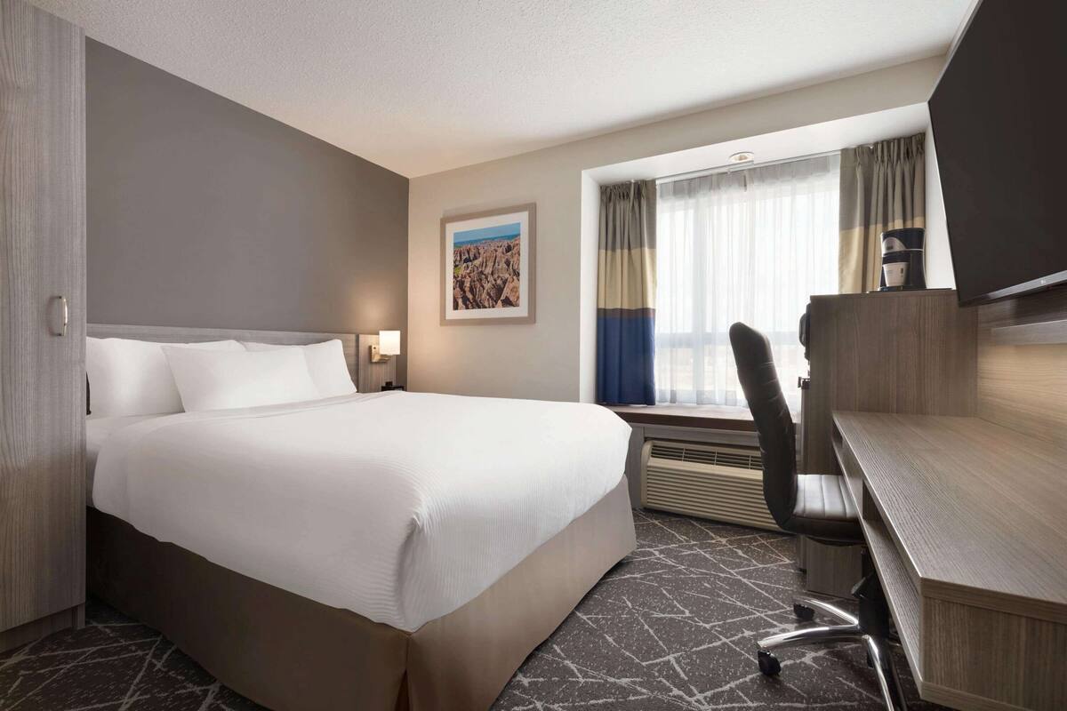 Une chambre d’hôtel avec un grand lit, un bureau avec une chaise, un téléviseur à écran plat et une fenêtre avec des rideaux.