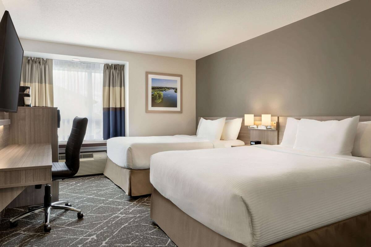 Une chambre d’hôtel avec deux lits, un bureau, une chaise, une télévision et une fenêtre avec des rideaux.
